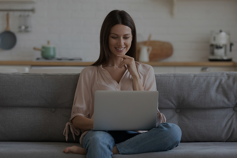 Smiling young woman using laptop, sitting on couch at home